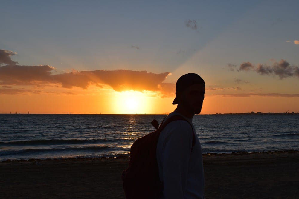 Puesta de Sol en Australia silueta de un chico con una gorra y detrás la puesta de sol en una playa